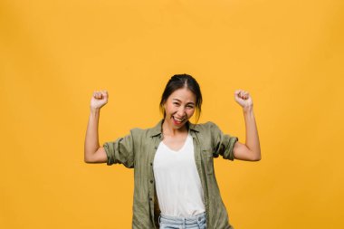 Olumlu ifadeli, neşeli ve heyecan verici, günlük giysiler içinde genç bir Asyalı kadın ve sarı arka plandaki kameraya bakın. Mutlu, sevimli, mutlu kadın başarıya sevinir. Yüz ifadesi kavramı.