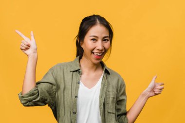 Neşeli bir ifadeyle gülümseyen Asyalı genç bir kadının portresi boş bir alanda, sarı arka planda izole edilmiş bir kameraya bakarak inanılmaz bir şey gösteriyor. Yüz ifadesi kavramı.