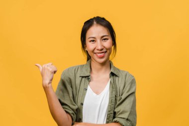 Neşeli bir ifadeyle gülümseyen Asyalı genç bir kadının portresi boş bir alanda, sarı arka planda izole edilmiş bir kameraya bakarak inanılmaz bir şey gösteriyor. Yüz ifadesi kavramı.