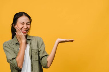 Neşeli bir ifadeyle gülümseyen Asyalı genç bir kadının portresi, boş bir alanda günlük giysiler içinde ve sarı arka planda izole bir şekilde duran inanılmaz bir şey gösteriyor. Yüz ifadesi kavramı.