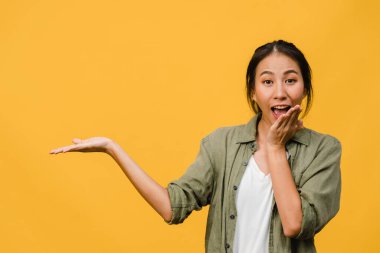 Neşeli bir ifadeyle gülümseyen Asyalı genç bir kadının portresi boş bir alanda, sarı arka planda izole edilmiş bir kameraya bakarak inanılmaz bir şey gösteriyor. Yüz ifadesi kavramı.