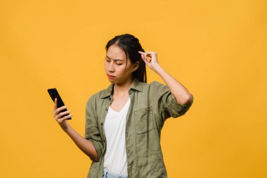 Asyalı genç bir bayanın telefonu olumlu bir ifadeyle kullandığını hayal etmek, günlük giysiler içinde mutluluğu hissetmek ve sarı arka planda izole bir şekilde durmak. Mutlu, mutlu, mutlu kadın başarıya sevinir..