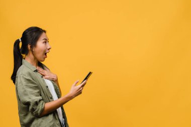 Asyalı genç bayanın cep telefonunu olumlu bir ifadeyle kullanmasına, geniş bir şekilde gülümsemesine, gündelik kıyafetler giymesine ve sarı arka planda tek başına durmasına şaşırdım. Mutlu, mutlu, mutlu kadın başarıya sevinir..