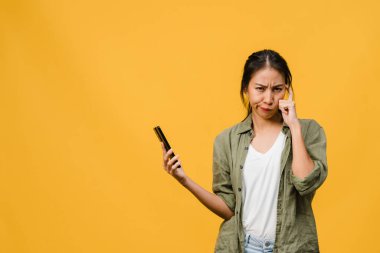 Asyalı genç bir bayanın telefonu olumlu bir ifadeyle kullandığını hayal etmek, günlük giysiler içinde mutluluğu hissetmek ve sarı arka planda izole bir şekilde durmak. Mutlu, mutlu, mutlu kadın başarıya sevinir..