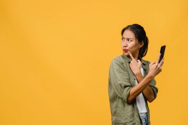 Asyalı genç bir bayanın telefonu olumlu bir ifadeyle kullandığını hayal etmek, günlük giysiler içinde mutluluğu hissetmek ve sarı arka planda izole bir şekilde durmak. Mutlu, mutlu, mutlu kadın başarıya sevinir..