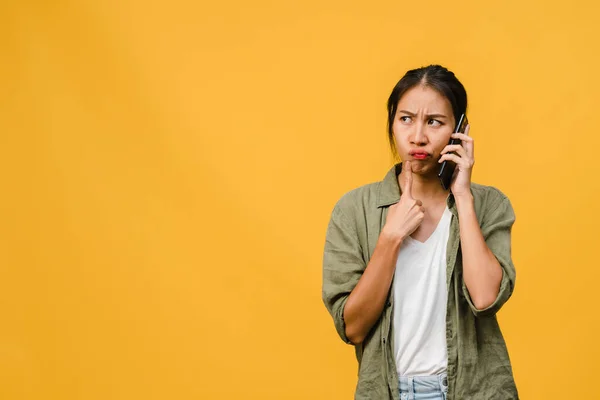 Young Asia lady talk by phone with negative expression, excited screaming, cry emotional angry in casual cloth and stand isolated on yellow background with blank copy space. Facial expression concept.