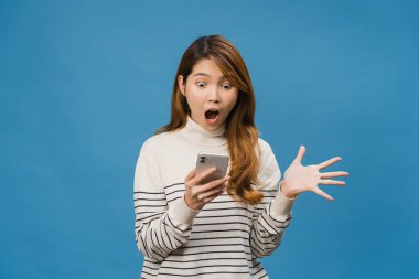 Asyalı genç bayanın cep telefonunu olumlu bir ifadeyle kullanmasına şaşırdım. Geniş bir gülümseme takınıyor, günlük kıyafetler giyiyor ve mavi arka planda tek başına duruyor. Mutlu, mutlu, mutlu kadın başarıya sevinir..