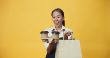 Sarı arka planda izole edilmiş müşterilere kahve ya da çay ikram eden önlüklü Asyalı mutlu bir gülümseme. Ticari paket servis kavramı.
