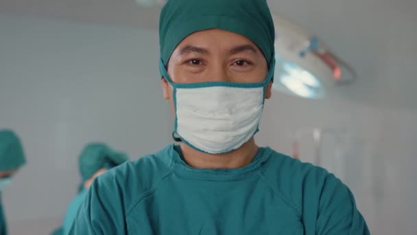 病院の手術室で患者に侵襲手術を行った後 若いアジア人アシスタントの男はカメラを見て微笑んだ プロの外科医 医療と医療のコンセプトの多様なチーム — ストック動画