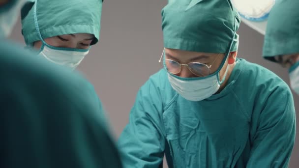 若いアジア人のアシスタントや看護師は 病院の手術室で患者に侵襲手術を行う プロの外科医 医療と医療のコンセプトの多様なチーム — ストック動画