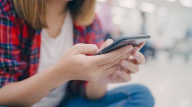 Kullanarak ve onun smartphone uçağının kalkış kapısı uluslararası havaalanında beklerken terminal Salonu sandalyede oturan süre kontrol mutlu Asyalı kadın. Kadınlar Havaalanı kavramında mutlu.