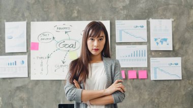 Başarılı yönetici iş kadınının portresi. Gündelik kıyafetlerle kameraya bakıp gülümsüyor. Modern ofis işyerinde kollarını kavuşturuyor. Genç Asyalı bayan birlikte çalışma alanında duruyor..
