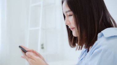 Genç Asyalı kadın uyan sabah, sonra yatakta yatıyordu süre Smartphone kullanarak gülümseyen güzel çekici Japon kız evde yatak odasında rahatlayın. Ev concept zaman yaşam tarzı kadınlar enjoying.