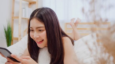 Akıllı telefon kontrol sosyal medya kontrol kullanarak genç Asyalı kadın sabah uyandıktan sonra yatakta yatarken mutlu gülümseyerek duygu, Güzel çekici Japon kız evde yatak odasında dinlenmek gülümseyen.