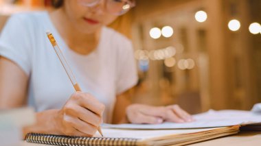Üniversitede kütüphanede kitap okuyan Asyalı kadın öğrenciler. Lisansüstü öğrencisi kız ödevlerini yapıyor, ders kitabı okuyor, ders çalışmak için üniversite kampüsünde fazla mesai yapıyor..