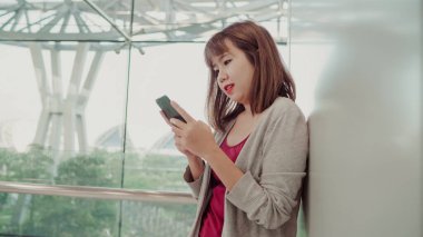 Kullanarak ve onun uçuş kurulu uçak kalkış kapısı için beklerken onu smartphone ayakta terminal salonunda kontrol çekici rahat mutlu Genç Asyalı kadın Uluslararası Havaalanı,.