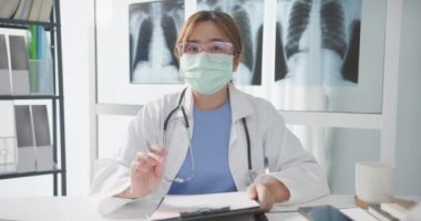 Stetoskoplu beyaz üniformalı genç Asyalı doktor hastayla bilgisayarlı konuşma videosu konferansı yapıyor ve sağlık hastanesindeki kameraya bakıyor. Danışmanlık ve terapi konsepti.