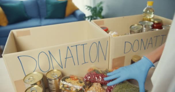 若いアジアの10代の少女ボランティアは 慈善財団で働いている間 食品や飲料の寄付を寄付用紙箱に梱包手袋を着用します ソーシャルワーカー フードバンク コロナウイルスの概念 — ストック動画