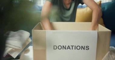 Mutlu genç Asyalı kız gönüllü olarak bağış kutusuna kıyafet paketliyor ve hayır kurumunda çalışıyor. Sosyal hizmet görevlisi, koronavirüs ve karantina konsepti. Yakın çekim..