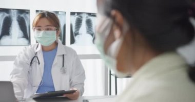 Genç Asyalı doktor, dizüstü bilgisayar kullanarak koruyucu maske takıyor. Haberler sunuyor. Hastane ofisindeki kız hastayla sonuçları ya da belirtileri tartışıyor. Corona virüsünden sonra yaşam tarzı yeni normal.