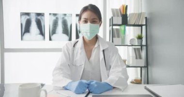 Kendine güvenen genç Asyalı doktor, sağlık hastanesindeki bir hastayla video konferans görüşmesinde kameraya bakıp gülümserken steteskopla koruyucu maske takıyor. Danışmanlık ve terapi konsepti.