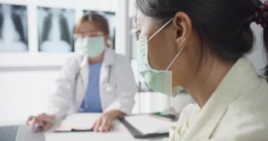 Genç Asyalı doktor, dizüstü bilgisayar kullanarak koruyucu maske takıyor. Haberler sunuyor. Hastane ofisindeki kız hastayla sonuçları ya da belirtileri tartışıyor. Corona virüsünden sonra yaşam tarzı yeni normal.