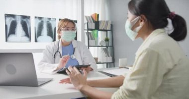 Genç Asyalı doktor, dizüstü bilgisayar kullanarak koruyucu maske takıyor. Haberler sunuyor. Hastane ofisindeki kız hastayla sonuçları ya da belirtileri tartışıyor. Corona virüsünden sonra yaşam tarzı yeni normal.