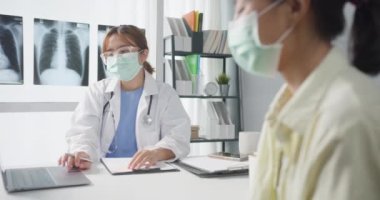 Kendine güvenen Asyalı doktor koruyucu yüz maskesi takıyor ve genç hasta kız sağlık kliniğinde ya da hastanede tıbbi danışmanlık yaparken kameraya bakıp gülümsüyor. Danışmanlık ve terapi konsepti.