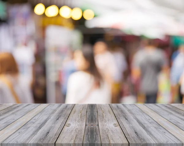Placa de madeira mesa vazia na frente de pessoas que fazem compras no mercado fundo justo. Perspectiva mercado de madeira e borrão - pode ser usado para exibir ou montar seus produtos - imagens de efeito vintage . — Fotografia de Stock