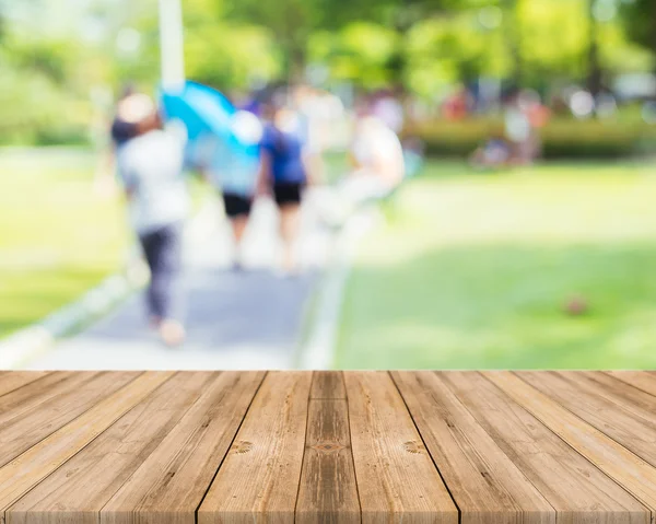 Holzbrett leerer Tisch vor verschwommenem Hintergrund. Perspektive braunes Holz mit verschwommenen Menschen Aktivitäten im Park - kann für die Anzeige oder Montage Ihrer Produkte verwendet werden. Frühlingszeit. — Stockfoto