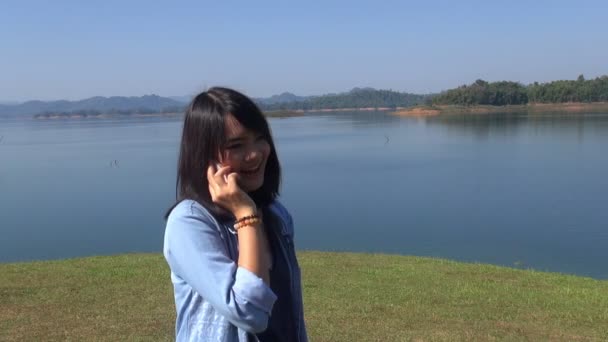 Sevimli genç kadın telefon gülümseme söz Gölü önünde dağlarda. — Stok video