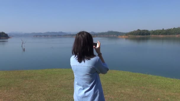 Joven mujer toma foto de la montaña del bosque una hermosa vista junto al lago — Vídeo de stock