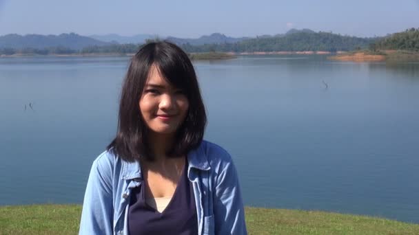 若い女性が湖のほとりに立っているし、カメラと笑顔に見える. — ストック動画