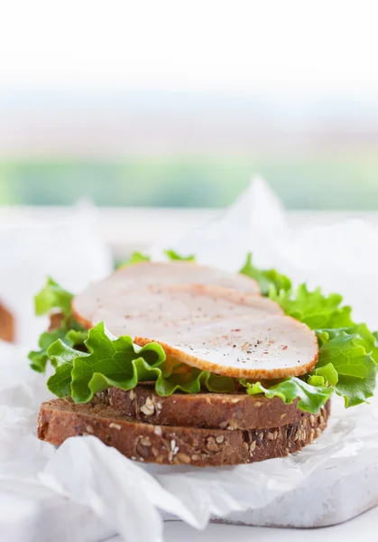 Hausgemachtes leckeres Sandwich mit Salatblättern und Schinken auf einem Schneidebrett auf Küchenhintergrund, mit Platz für Text, selektiver Fokus — Stockfoto