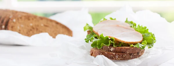 Homemade tasty sandwich with salad leaves and ham on a cutting board on a kitchen background, closeup, selective focus