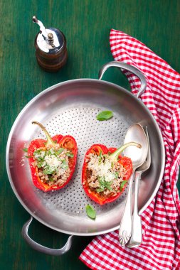 Stuffed vegetarian or vegan filled red paprika or bell pepper with spelt or brown rice and vegetables with cheese and fresh basil on a fried pan on a vintage wooden green background, top view