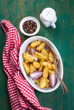 Oven-baked cut potato with red onion and Italian herbs, rustic, vintage or country style in a round bowl with red napkin on an old vintage green wooden background, top view