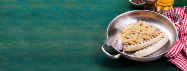 White grilled sausages with sauerkraut or cabbage, black pepper and fresh cold beer in a vintage pan on an old vintage green wooden background with free place for text, closeup, horizontal