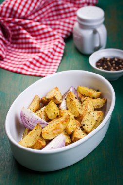 Oven-baked cut potato with red onion and Italian herbs, rustic, vintage or country style in a round bowl on an old vintage green wooden background, top view, with free space for text