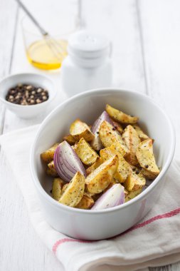 Oven-baked cut potato with red onion and Italian herbs, rustic, vintage or country style in a round bowl with white napkin on an old vintage wooden background, closeup
