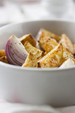 Oven-baked cut potato with red onion and Italian herbs, rustic, vintage or country style in a round bowl with white napkin on an old vintage wooden background, closeup