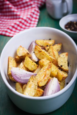 Oven-baked cut potato with red onion and Italian herbs, rustic, vintage or country style in a round bowl on an old vintage green wooden background, top view, with free space for text