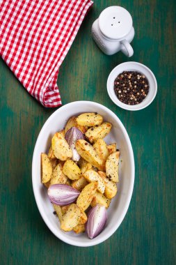Oven-baked cut potato with red onion and Italian herbs, rustic, vintage or country style in a round bowl on an old vintage green wooden background, top view, with free space for text