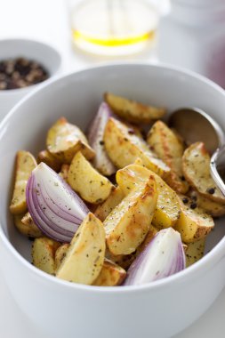 Oven-baked cut potato with red onion and Italian herbs, rustic, vintage or country style in a round bowl with white napkin on an old vintage wooden background, closeup