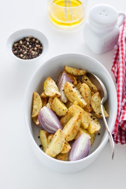 Oven-baked cut potato with red onion and Italian herbs, rustic, vintage or country style in a round bowl with white napkin on an old vintage wooden background, closeup