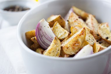 Oven-baked cut potato with red onion and Italian herbs, rustic, vintage or country style in a round bowl with white napkin on an old vintage wooden background, closeup