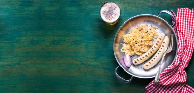 Beyaz ızgara sosis lahana veya lahana, siyah biber ve soğuk bira eski, yeşil ahşap bir arka planda eski bir tavada, yazı için boş alan, üst görünüm