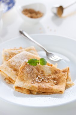 French crepes or pancakes with sugar powder, nuts and fresh mint on a white plate on a white background for breakfast, closeup