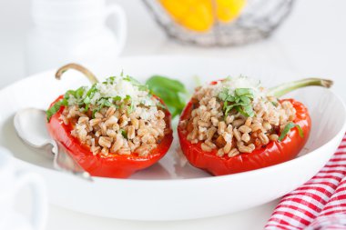 Stuffed vegetarian or vegan filled red paprika or bell pepper with spelt or brown rice and vegetables with cheese and fresh basil on a white plate on a kitchen background, closeup clipart