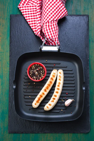 Saucisses grillées blanches au poivre noir dans une poêle à griller avec serviette rouge sur un vieux fond de bois vert vintage, vue sur le dessus — Photo